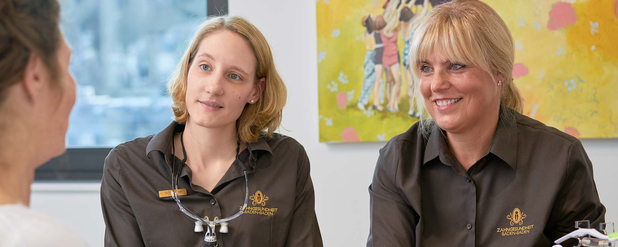 Bei einer Zahnprophylaxe in der Zahnarztpraxis Zahngesundheit Baden-Baden werden sie von ausgewiesenen Prophylaxeassistentinnen behandelt. Das Bild zeigt zwei junge Frauen als ZFA, die mit einem Patienten die individuelle Prophylaxe und Professionelle Zahnreinigung bereden.