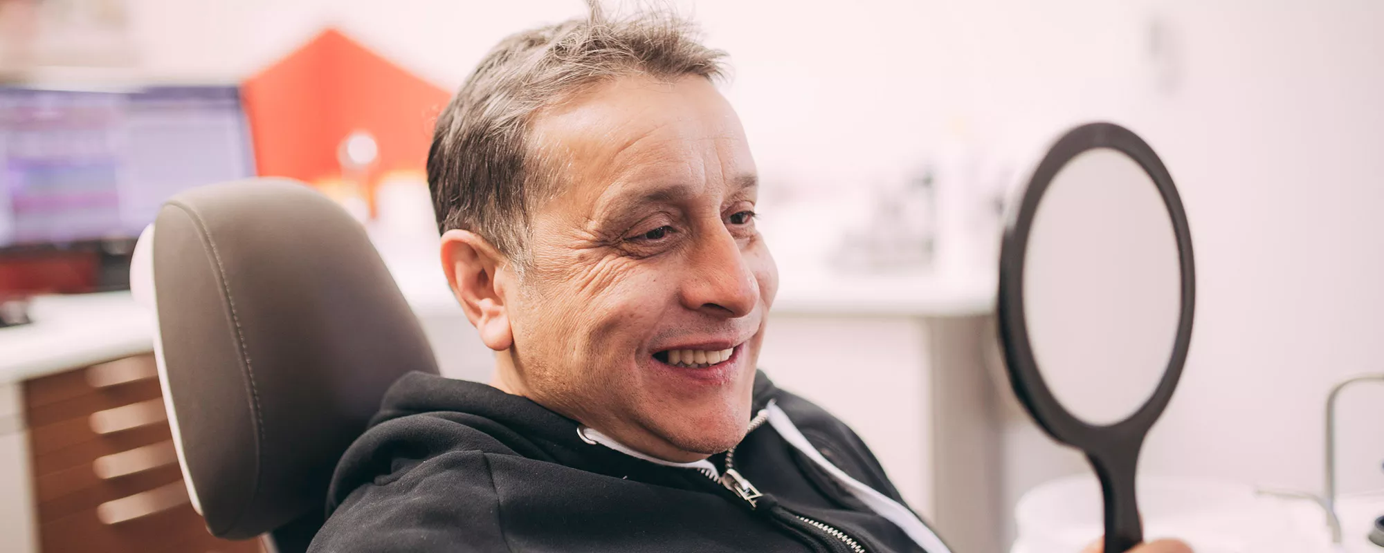 Patient betrachtet sein Lächeln im Spiegel nach Zahnbehandlung